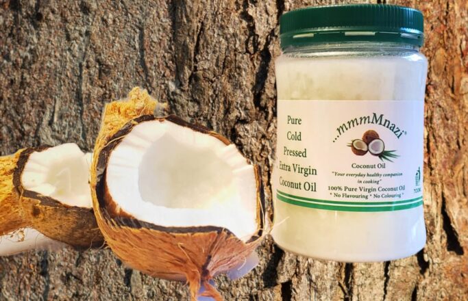 Cold pressed coconut oil beside cracked coconut halves
